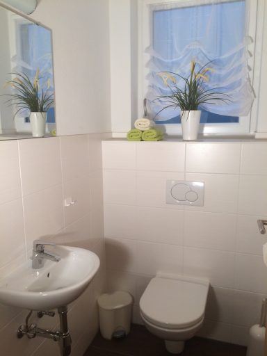 Helles Badezimmer mit Waschbecken, Toilette, Pflanzen und Fenster.